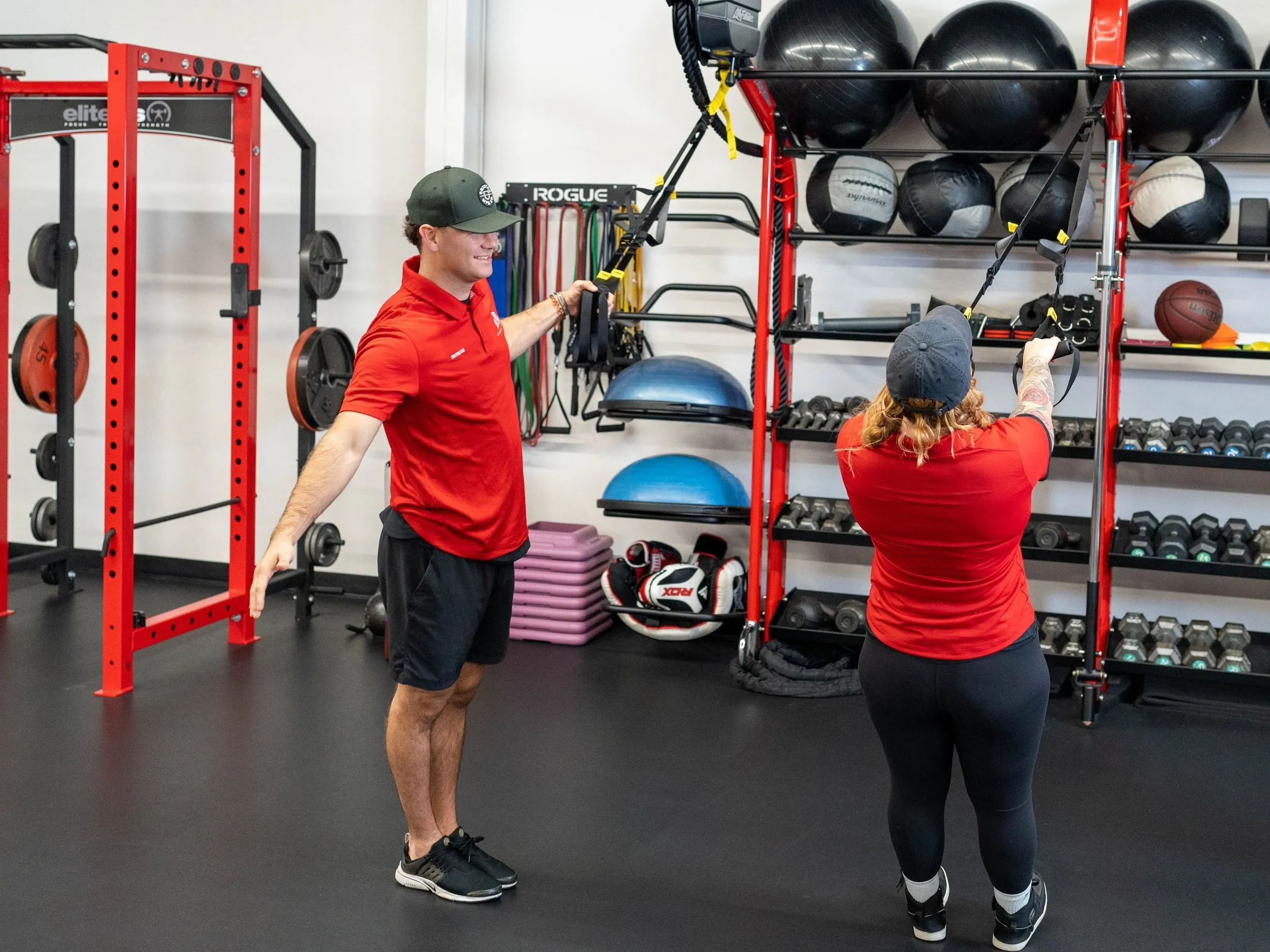 A trainer coaching a member through a suspension-strap exercise