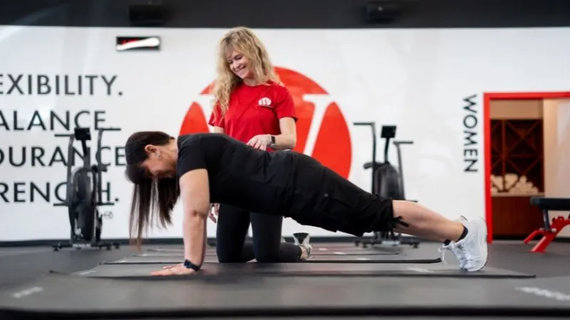 A trainer guiding a member through a plank on the mat